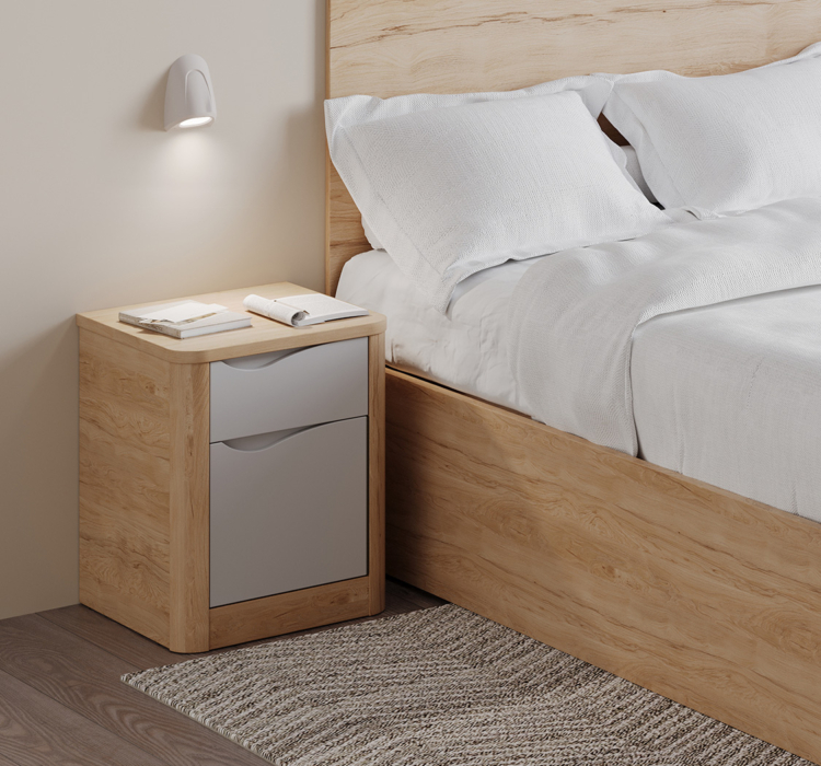 Table de chevet Acumen en bois clair avec deux tiroirs gris, placée à côté d’un lit double dans une chambre de soins sécurisée