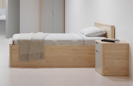 Table de chevet Acumen en bois clair avec façades de tiroirs grises, conçue pour accompagner les lits simples dans les environnements médico-sociau