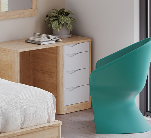 Bureau Acumen en bois clair avec tiroirs blancs et poignées intégrées, installé dans une chambre de soins avec fauteuil turquoise.
