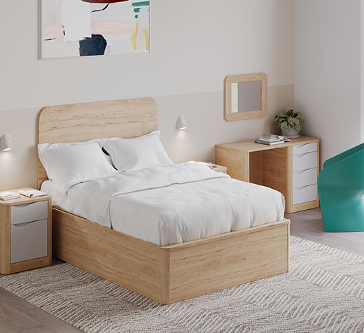 Lit double Acumen en bois clair avec tête de lit assortie, accompagné d’un bureau, d’une table de chevet et d’un miroir mural dans une chambre de soins sécurisée.