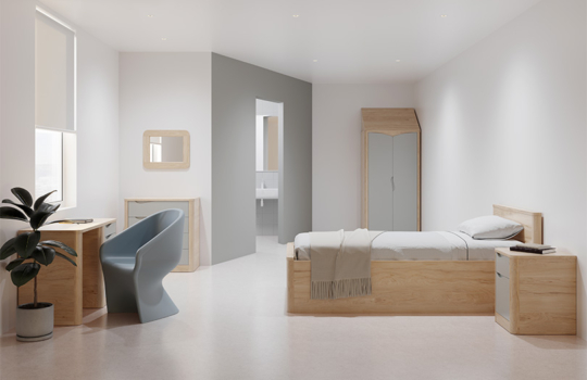 Lit simple Acumen en bois clair avec armoire, bureau et table de chevet assortis, dans une chambre de soins médico-sociale.