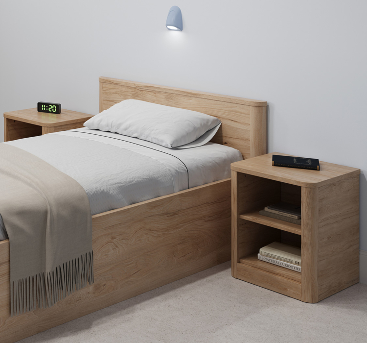 Table de chevet ouverte Acumen en bois clair avec deux étagères, placée à côté d’un lit dans une chambre médico-sociale.