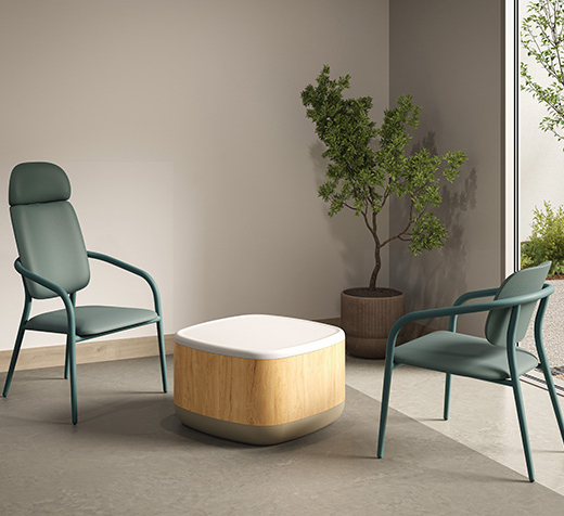 Deux chaises Appa Lounge à structure métallique avec dossier bas et haut, disposées autour d’une table basse en bois clair, dans un espace de détente lumineux adapté aux environnements de soins.