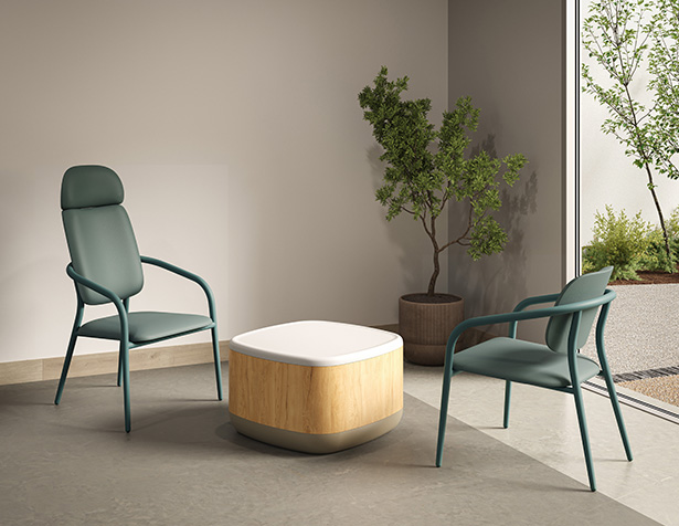 Deux chaises Appa Lounge à structure métallique avec dossier bas et haut, disposées autour d’une table basse en bois clair, dans un espace de détente lumineux adapté aux environnements de soins.